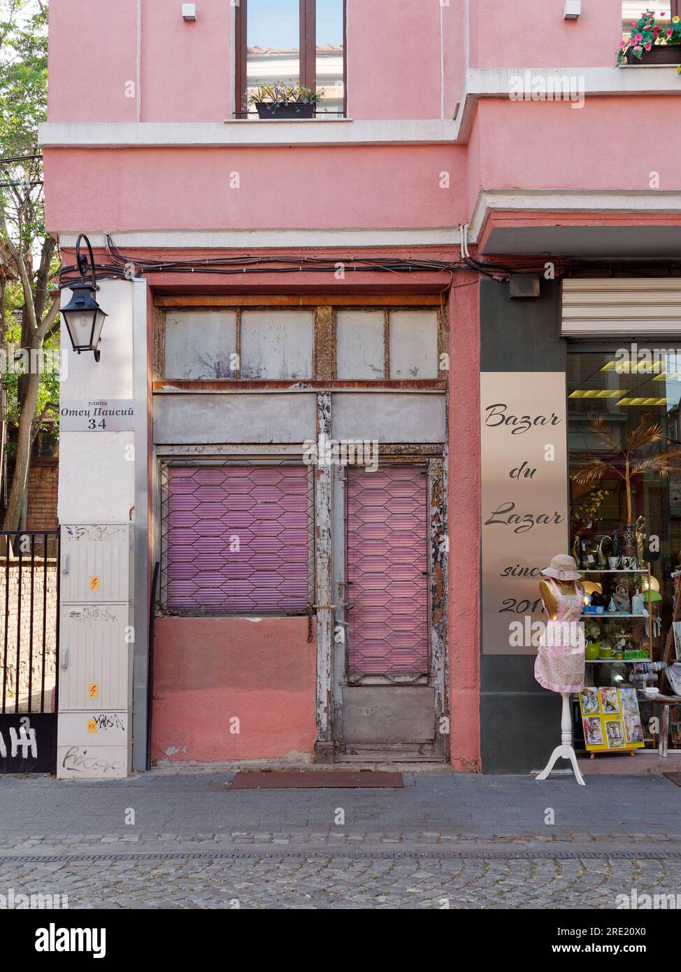 Peach and pink coloured building with pink shutters beside a shop with a pink outfit. Plovdiv, Bulgaria, July 24, 2023. Stock Photo