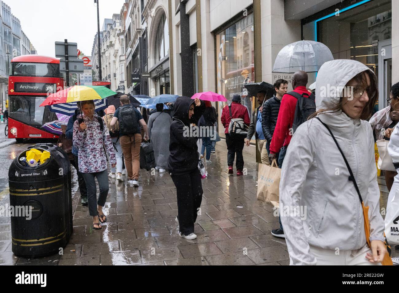 Tourists on Oxford Street in London's West End shelter form the heavy summer rain showers underneath umbrellas whilst shopping, England, UK Stock Photo