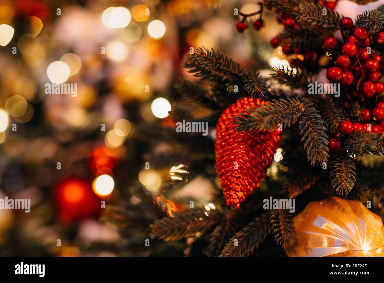 Red berries and pine cone hanging on the Christmas tree. Creative details and golden magic bokeh lights on background. Winter holiday decorations Stock Photo