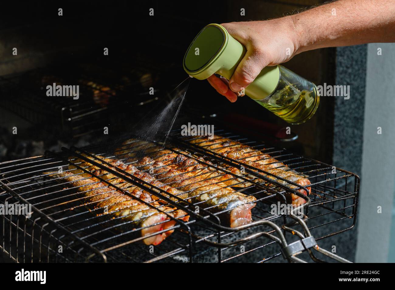 Fish is baked on a metal grill in a flame of fire. The hand sprinkles with olive oil, spices fish, baked on the grill. Stock Photo