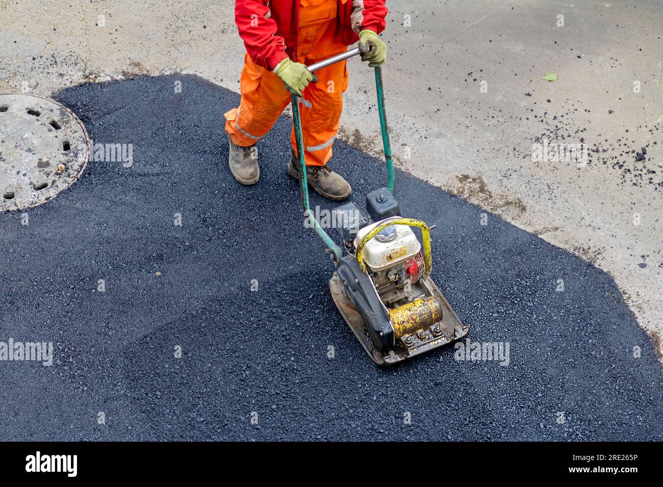 Man using vibratory plate compactor working on paving asphalt on a