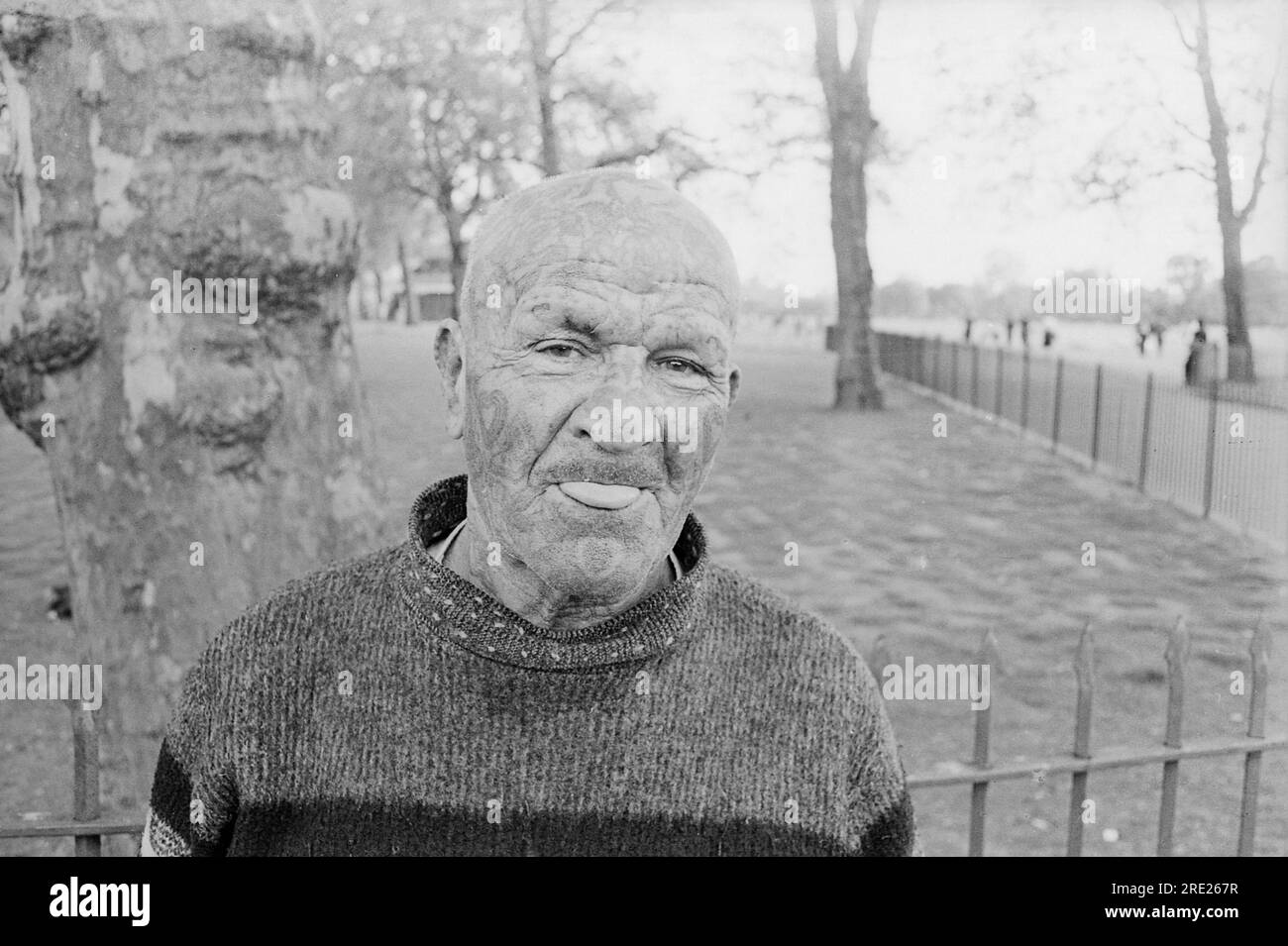 London. 1965 – The enigmatic ‘Tattoo Man’, Jacobus Petrus Van Dyn (1896-1983) posing for a photograph at Speaker’s Corner, Hyde Park , whilst poking his tongue out. Official records show that Van Dyn was born in Cradock, South Africa, had enlisted into the British army during the First World War and was later employed as a merchant seaman.  He had a string of criminal convictions going back as far as 1908 and made regular appearances at Speaker’s Corner, where he would recall colourful accounts of his life, claiming that he had once worked as a driver for the American gangster Al Capone. Stock Photo