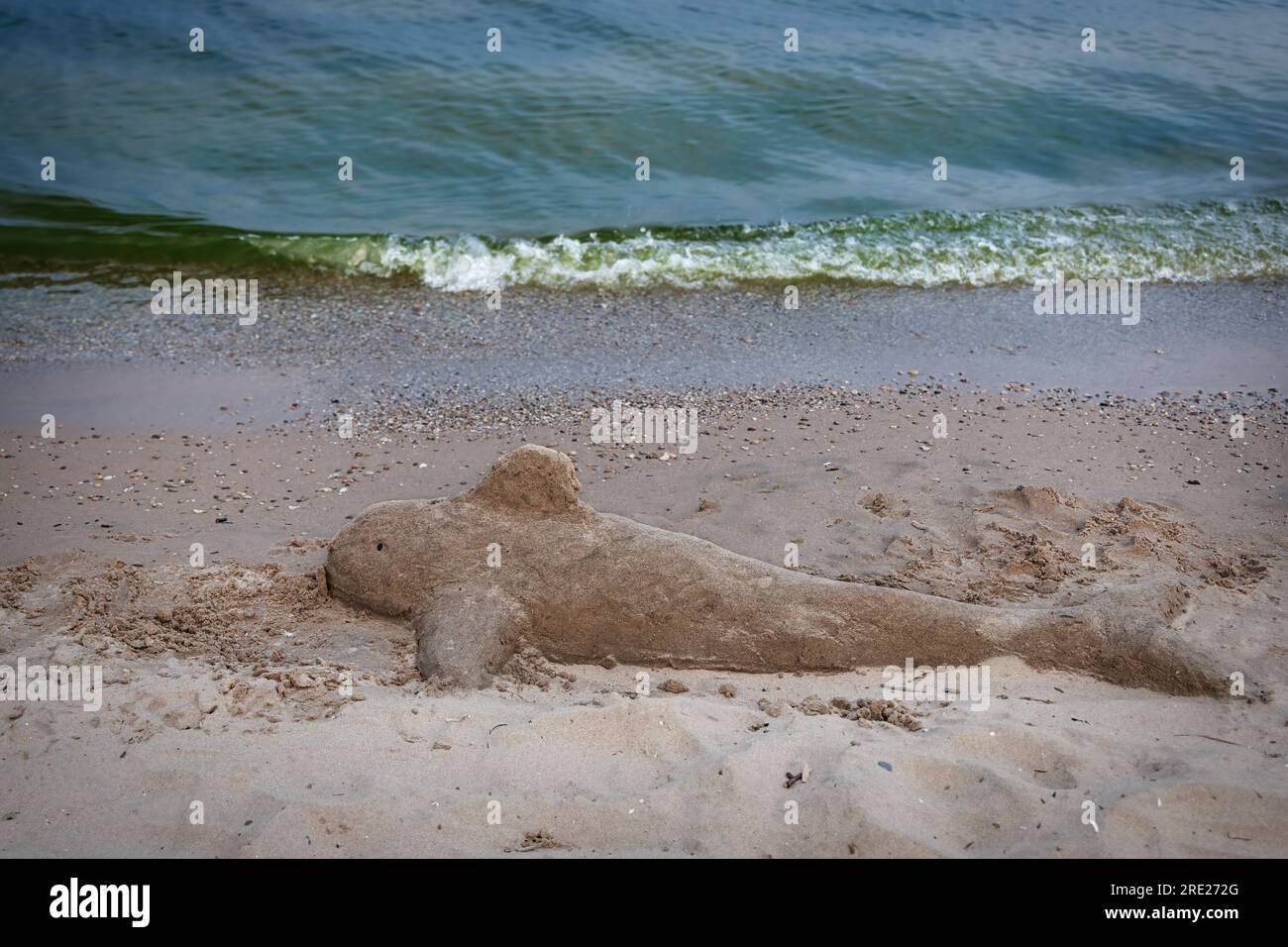 A sand sculpture of a dolphin, left by visitors to a sand sculpting festival, begins to wash away on shores of Lake Michigan at Manitowoc, Wisconsin. Stock Photo