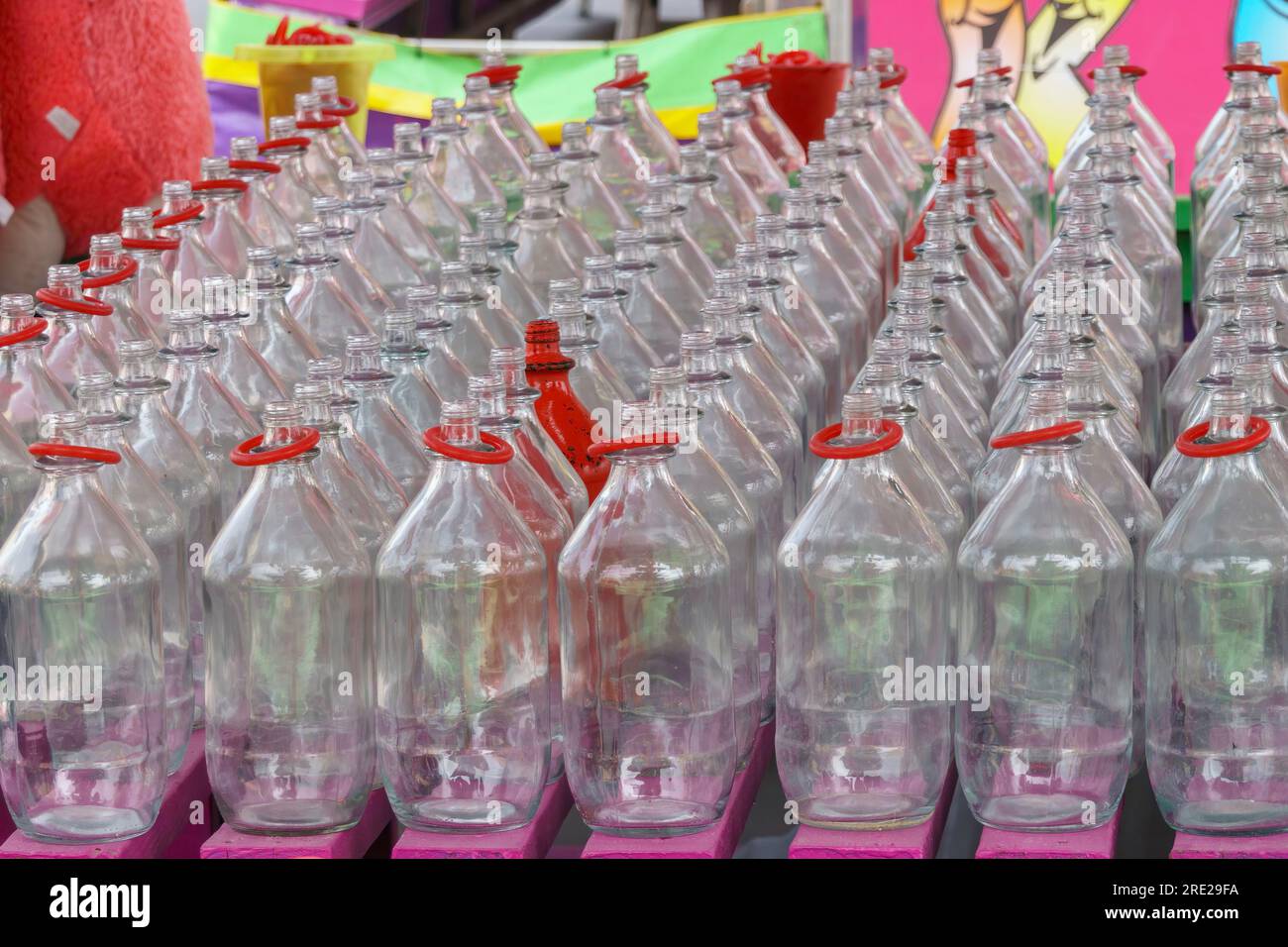 Rows of glass bottles for a carnival ring toss game. Many have red