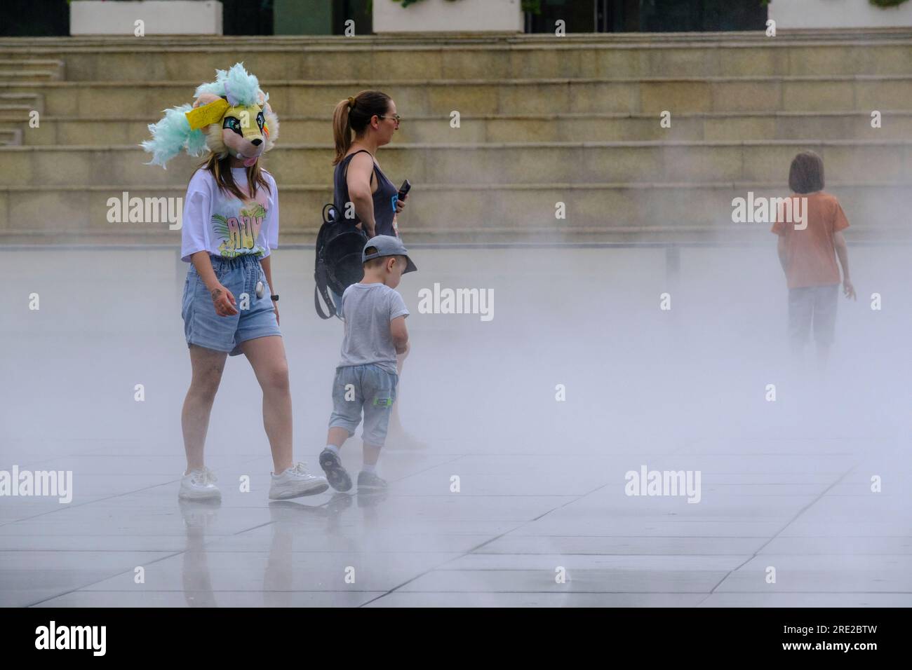 Kazakhstan, Almaty. Women and Child Walk through 'Fog Fountain' in front of Entrance to Caspian University. Stock Photo