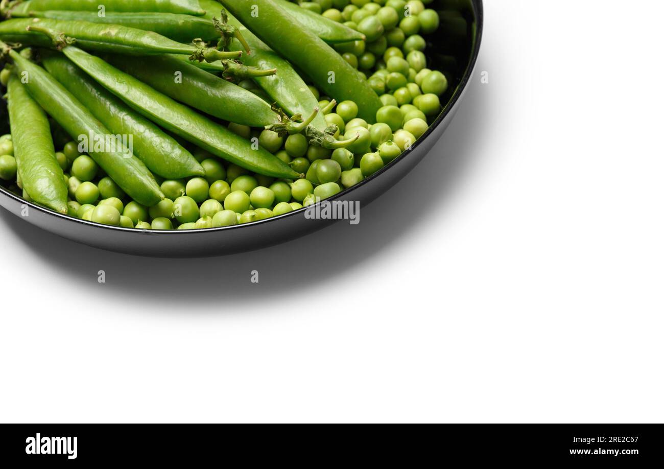 Fresh green peas in pods and peeled green pea seeds in a black round plate, isolated on white background. Vegetable protein, healthy products. Stock Photo