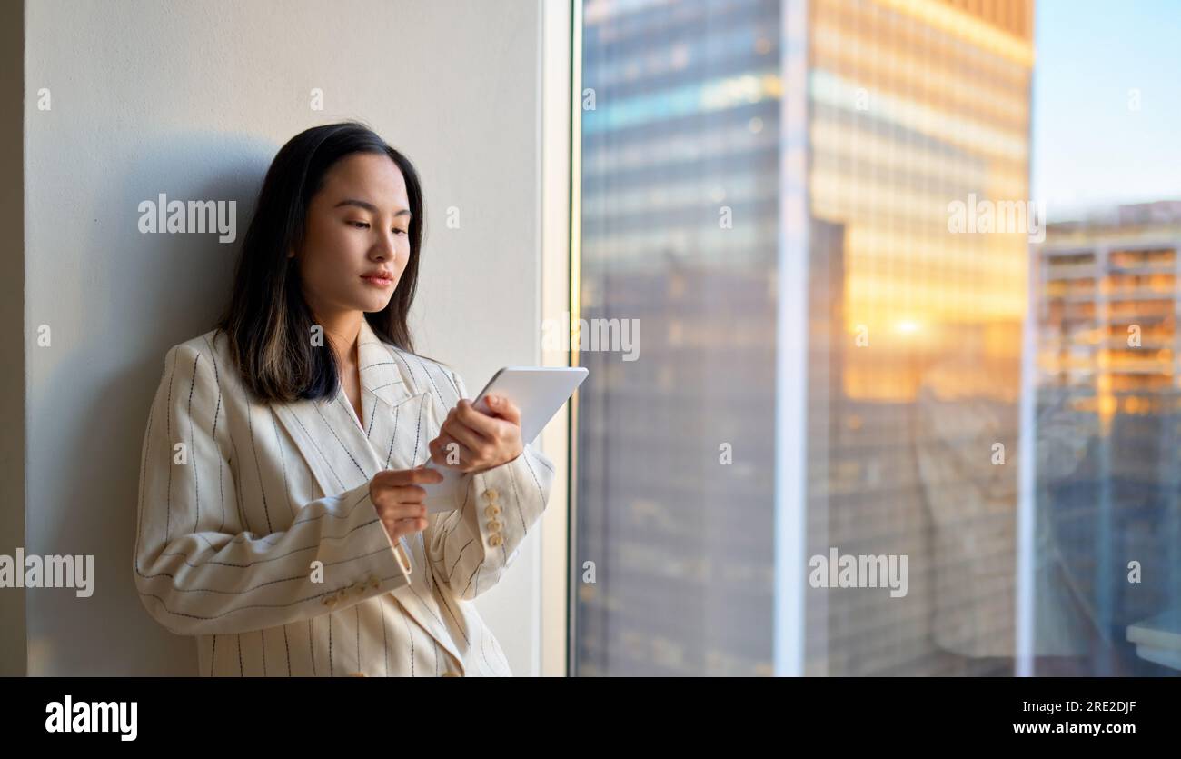Young Asian business woman executive using tablet standing in office at window. Stock Photo