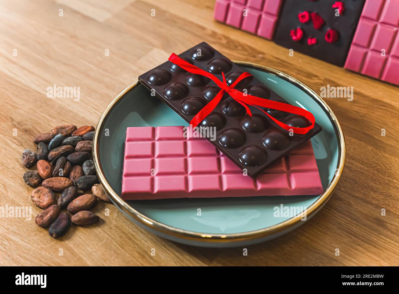 Bars of ruby and dark chocolate artfully arrenged on blue plate. Premium chocolate tied with red ribbon presented next to cocoa seeds. High quality photo Stock Photo