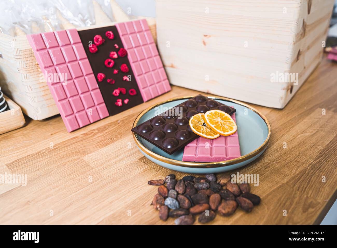 Closeup indoors shot of selection of dark and ruby chocolate with dried raspberries and oranges. Different-shaped bars of chocolate. Sweets and candy concept. Chocolate on blue plate on wooden table with chocolate beans.. High quality photo Stock Photo
