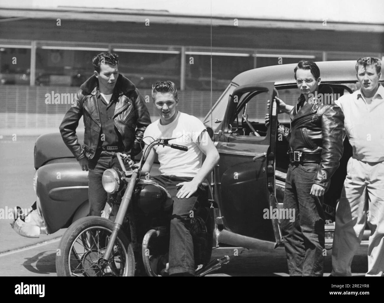 San Francisco, California  c. 1954 Four tough looking teenage youths with ducktail haircuts, leather jackets, and a motorcycle hanging out in a parking lot. Stock Photo