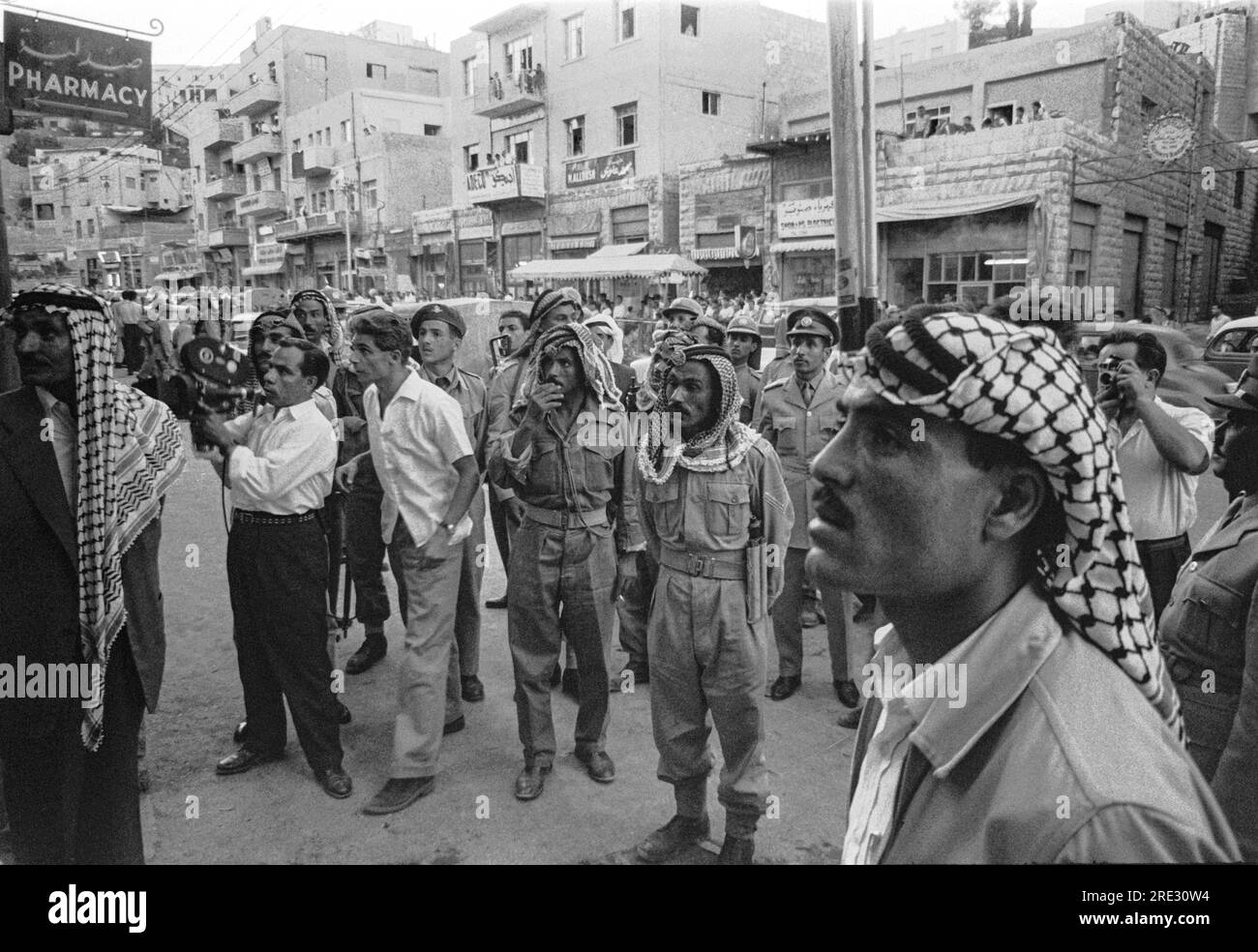 Amman, Jordan:  July, 1958 Men and soldiers gathered on a street intently watching something in a storefront window, possibly news reports of the overthrow of King Faissal by Saddam Hussein  in neighboring Iraq. Stock Photo