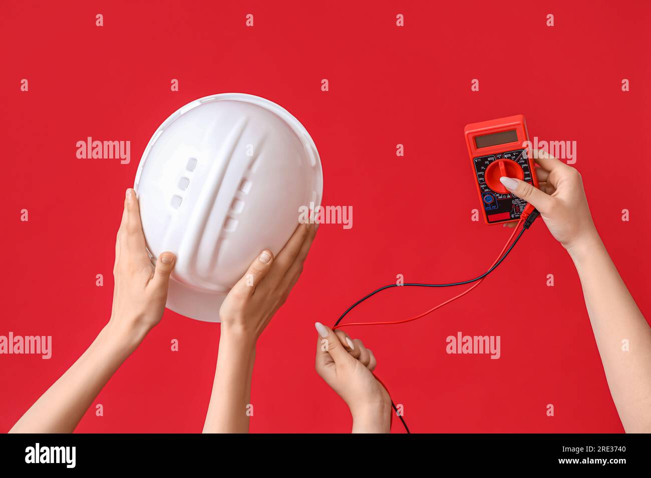 Electrician hands with hardhat and multimeter on red background Stock Photo