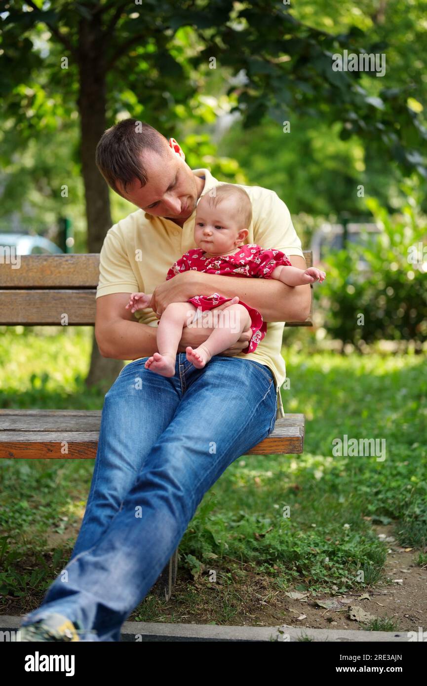 Father sitting on a bench in the park and holding his little baby girl Stock Photo