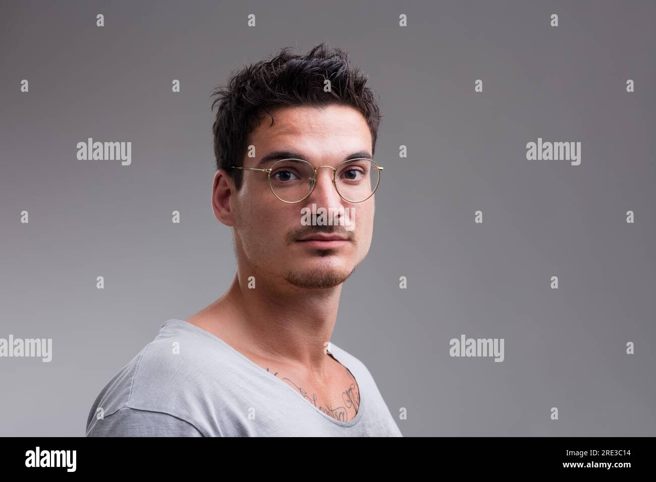 Handsome young man, short hair, glasses, revealing chest tattoo through short-sleeved shirt. His serious, uncertain gaze questions his future and iden Stock Photo