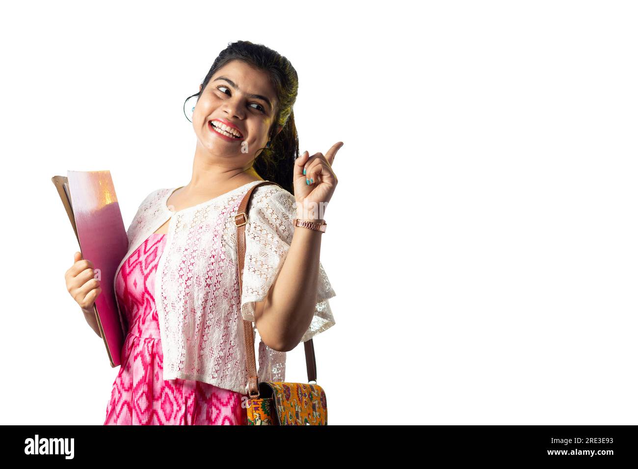 A pretty young Indian girl with books in hand pointing with smiling ...