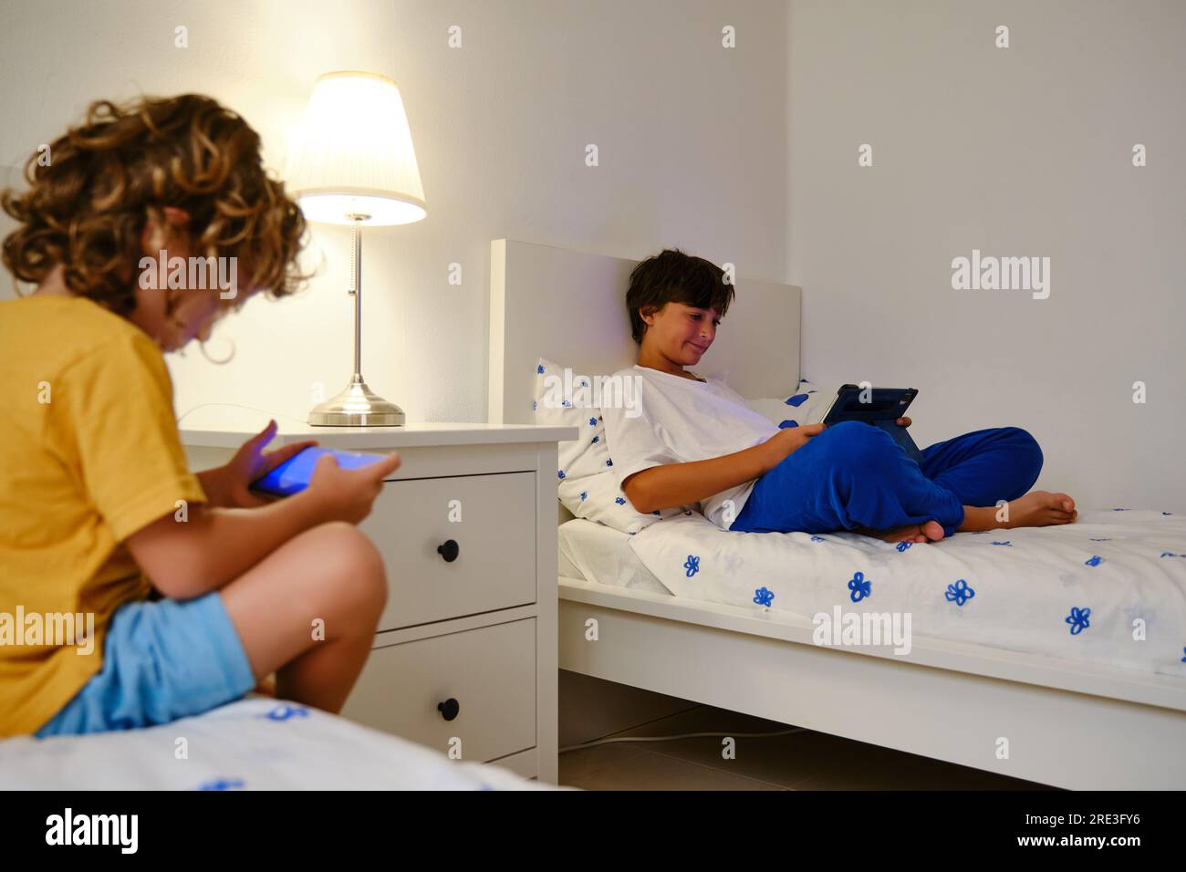 Brothers using gadgets in bedroom Stock Photo