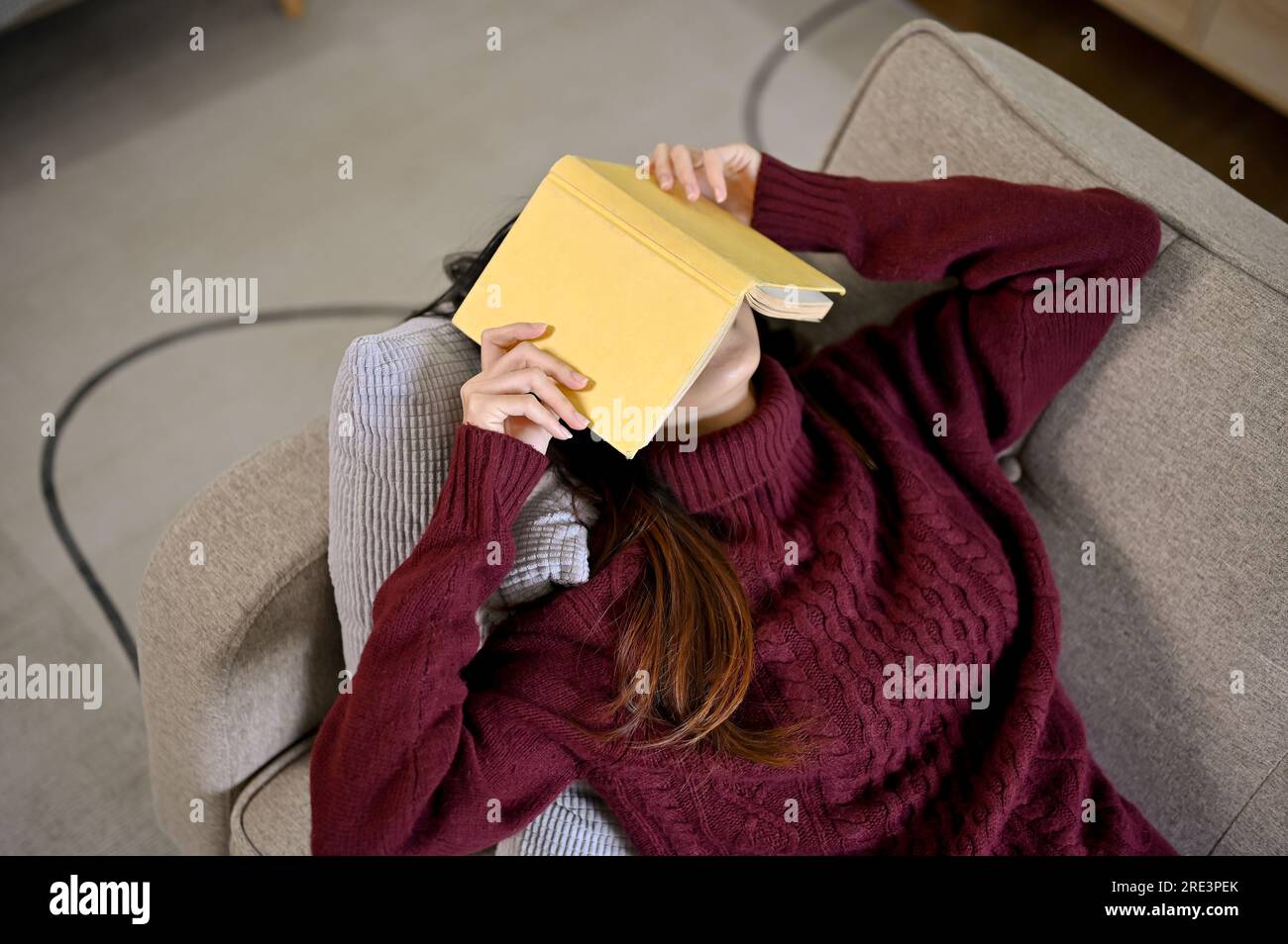 Young Asian woman laying down on the sofa with book cover on her face, taking a nap, relaxing in free time Stock Photo