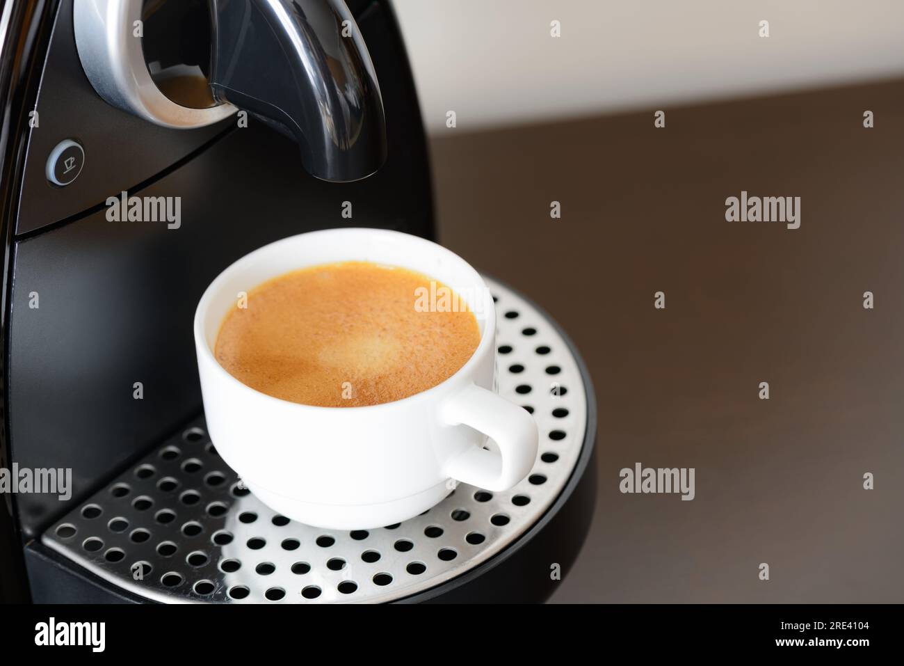 https://c8.alamy.com/comp/2RE4104/a-coffee-machine-and-a-white-cup-with-coffee-is-placed-on-the-wooden-table-2RE4104.jpg