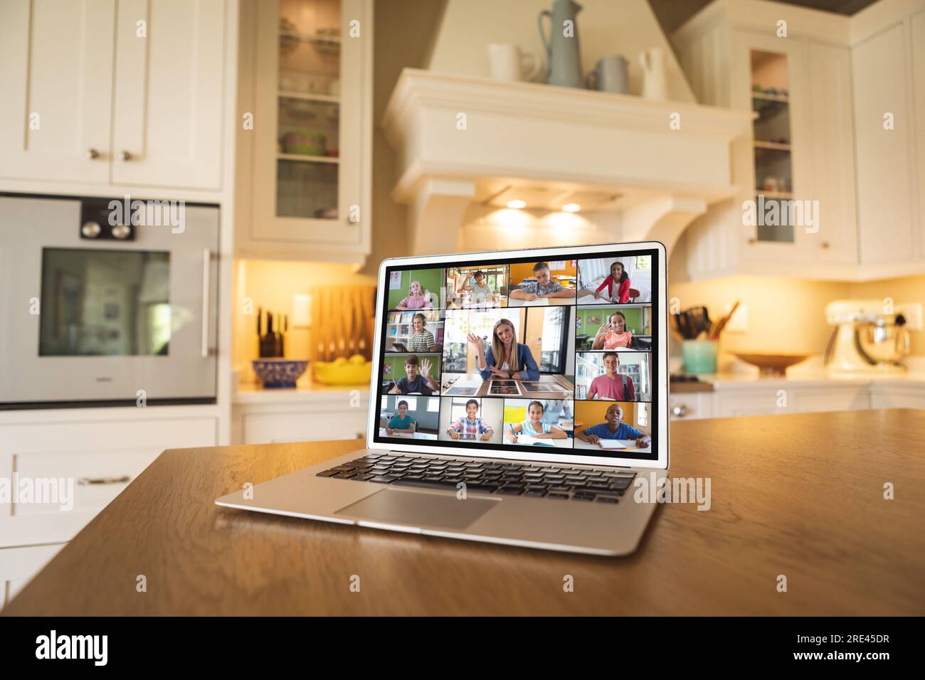 Laptop with video conference with caucasian female teacher and diverse students on kitchen table Stock Photo