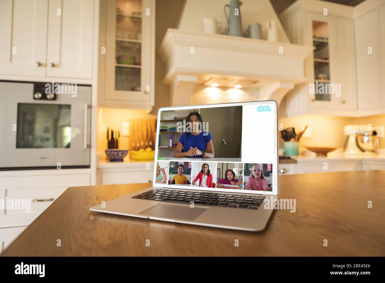 Laptop with video conference with biracial female teacher and diverse students on kitchen table Stock Photo