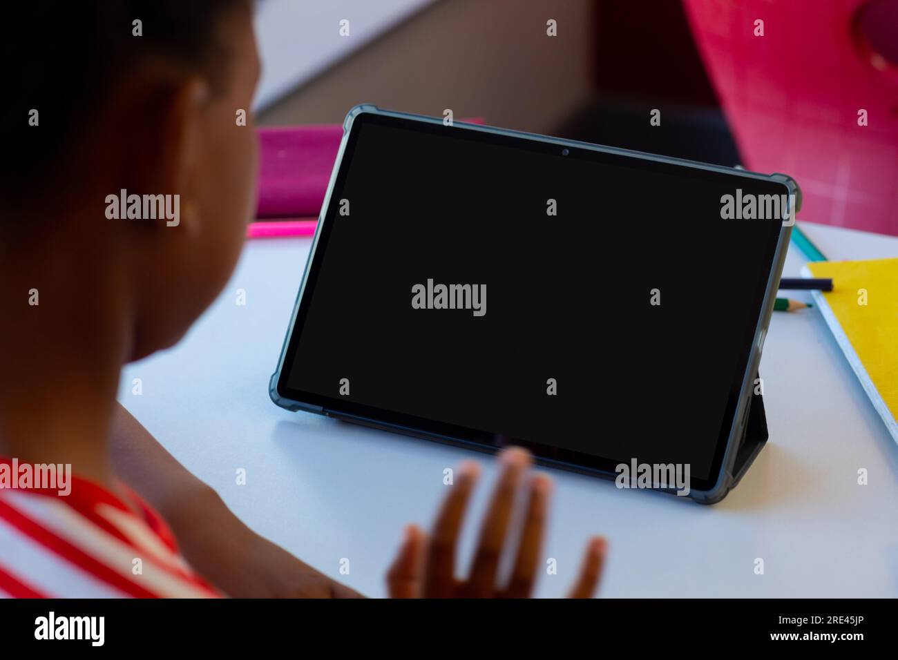 Biracial schoolgirl waving hand and having tablet video call with copy space Stock Photo