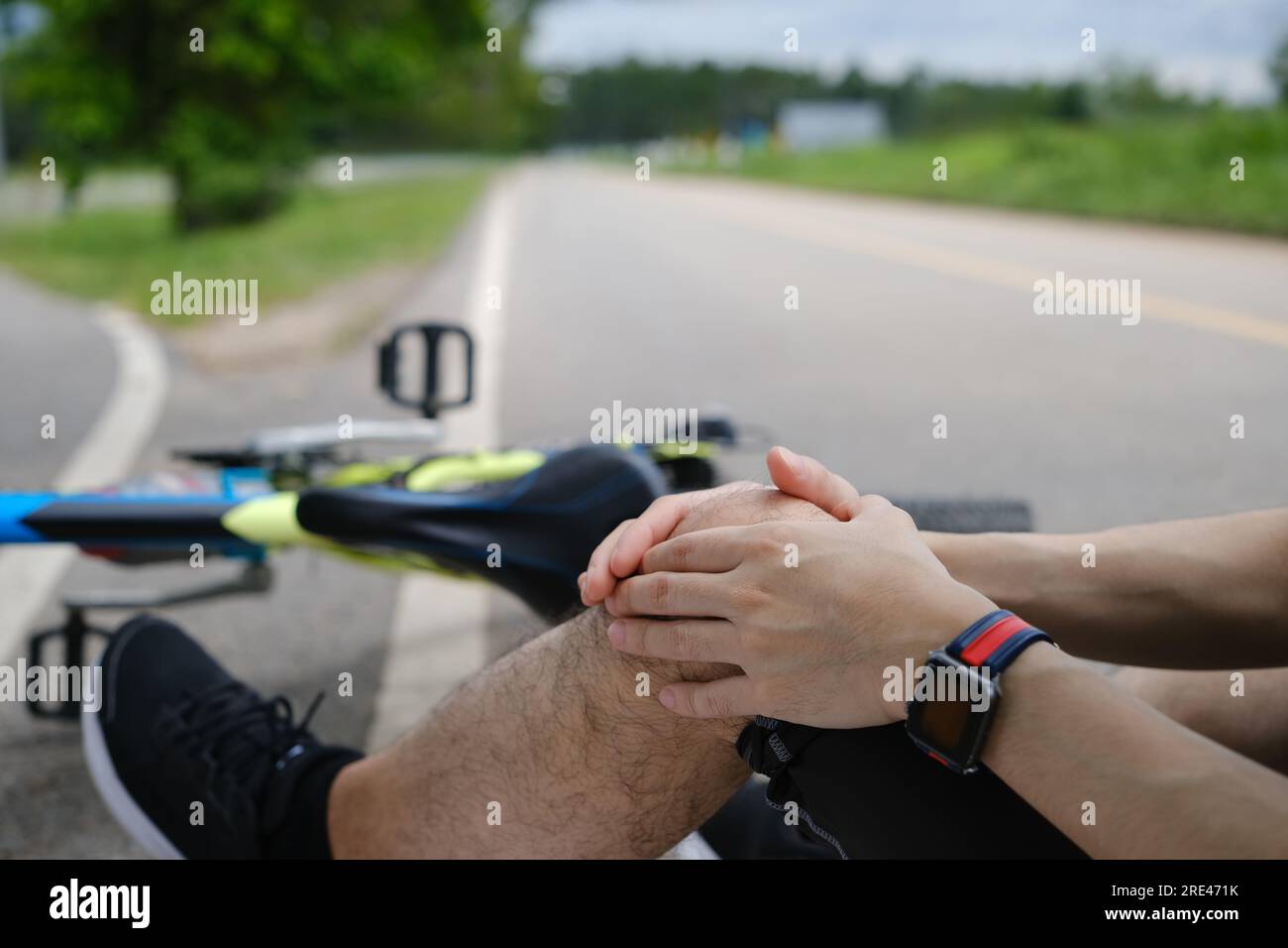 Man with injured knee sitting near bicycle outdoors, falling down from bicycle. Concept accident
