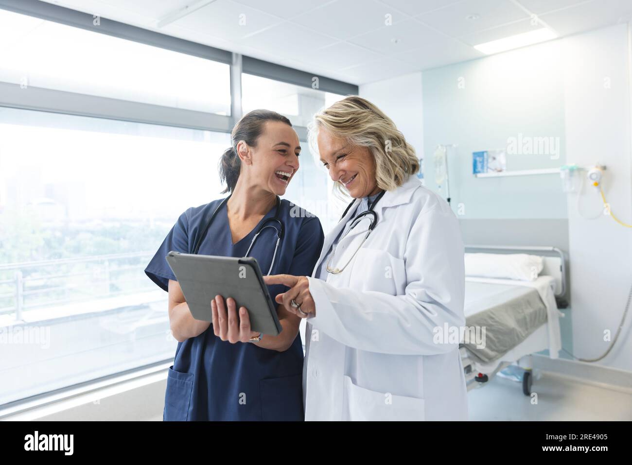 Happy caucasian female doctors with stethoscopes using tablet at hospital Stock Photo