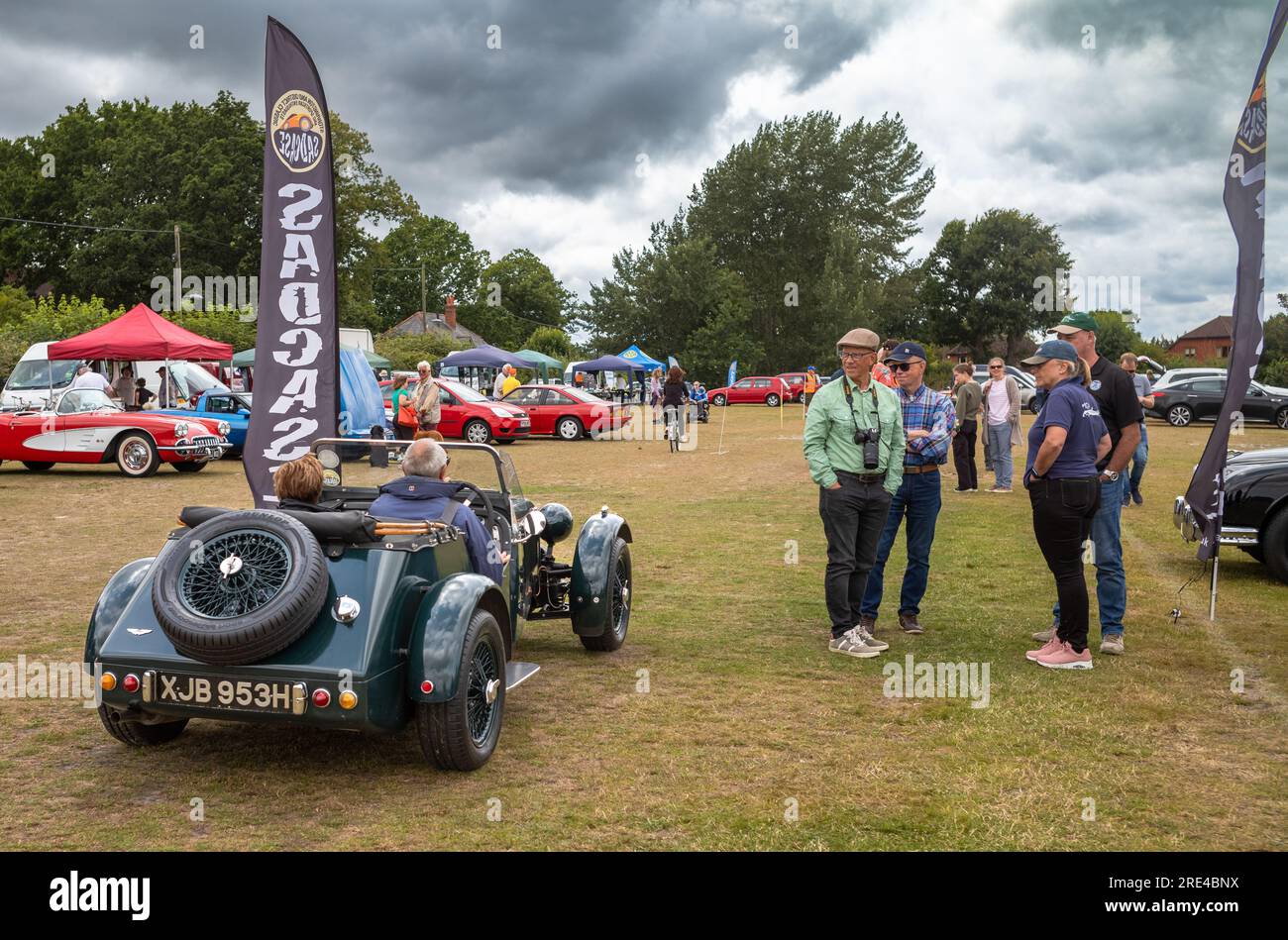 Car enthusiasts watch a  participant drive his 2-seater dark green NG TD kit car (XJB 953H) from a classic car show in Storrington, West Sussex, UK. Stock Photo