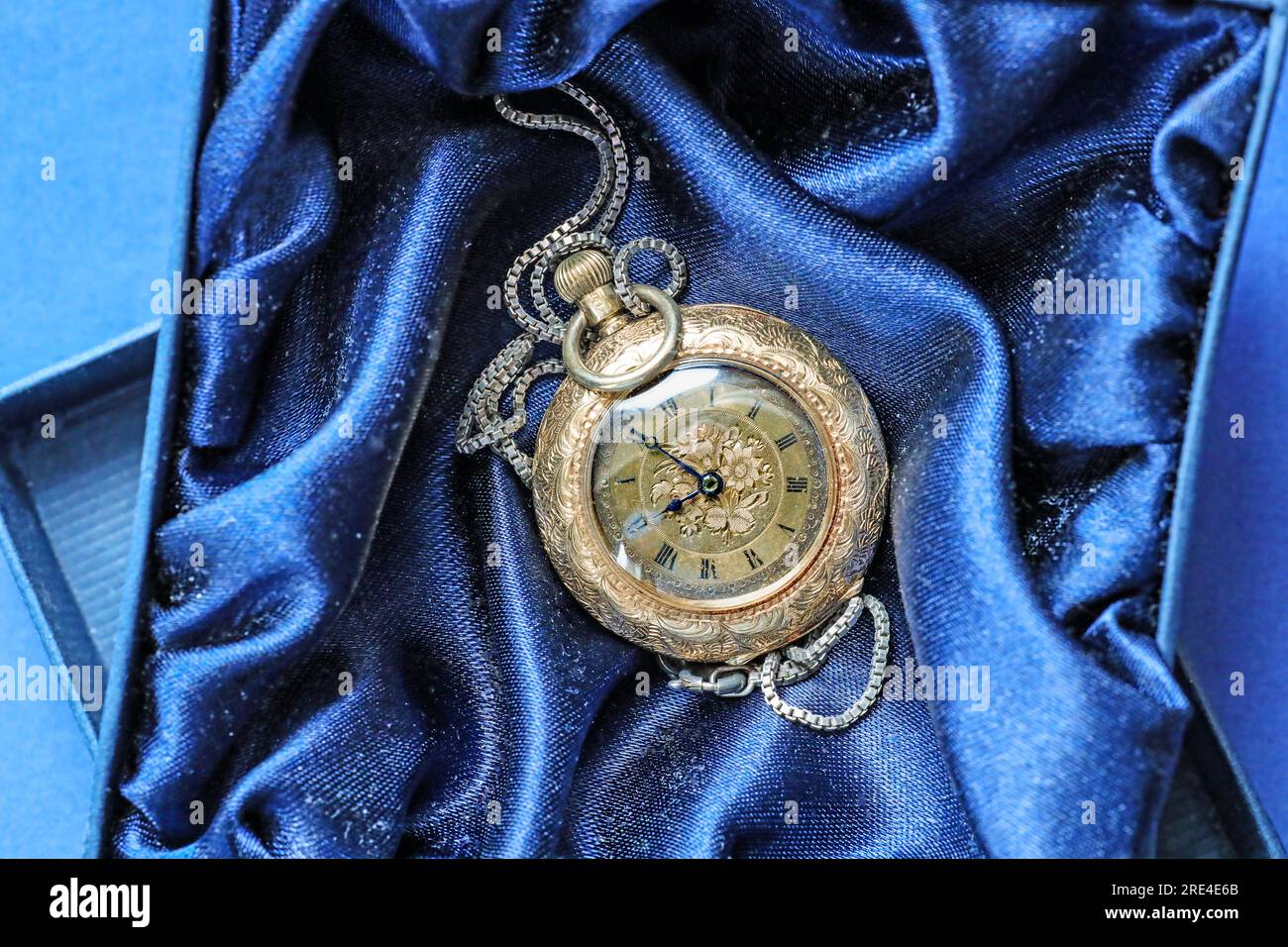 A gold fob watch on a silken blue background. Roman numerals on the