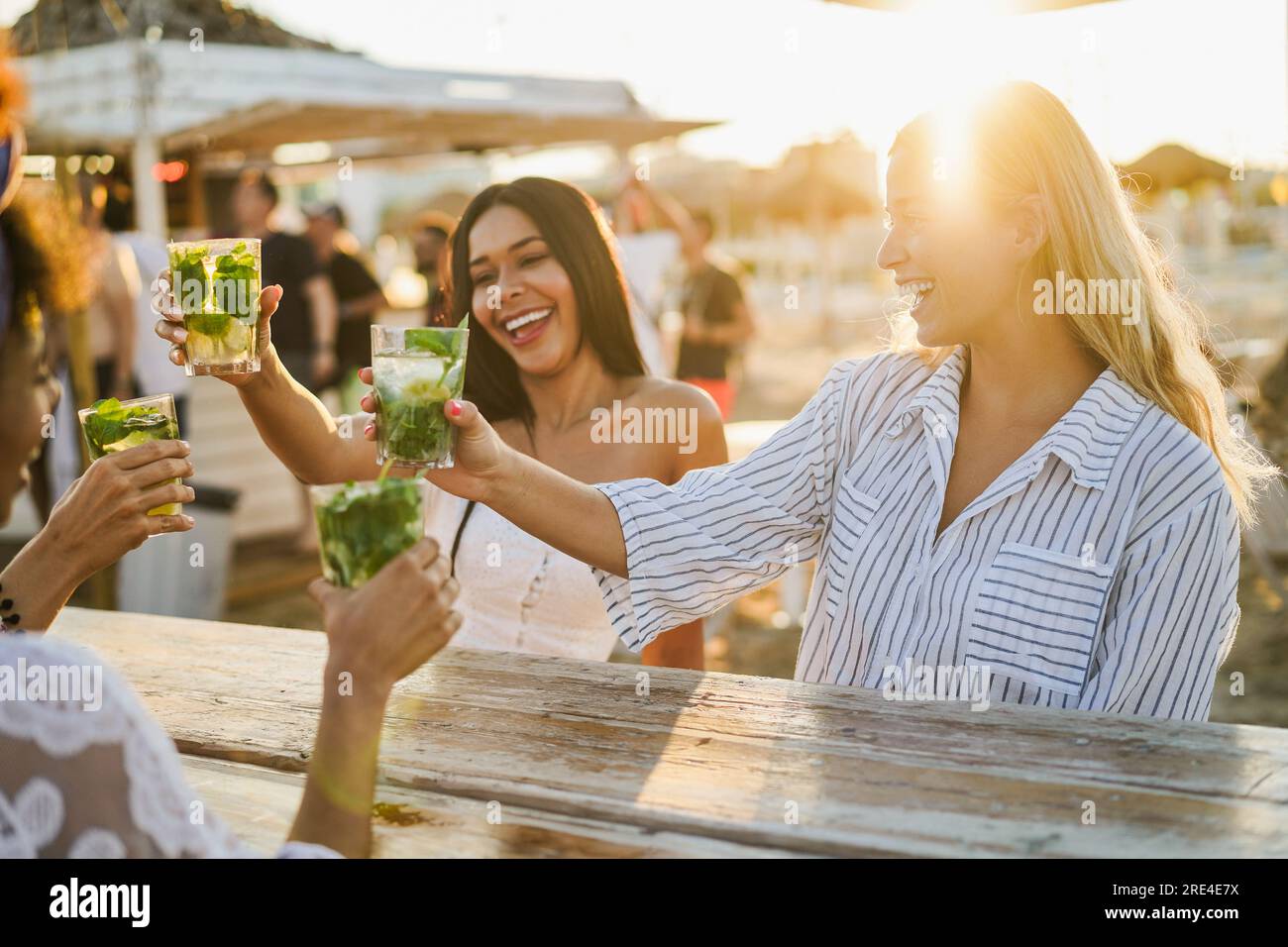 Happy girls cheering with mojitos on the beach at chiringuito sunset party - Summer vacation and people lifestyle concept - Main focus on right female Stock Photo