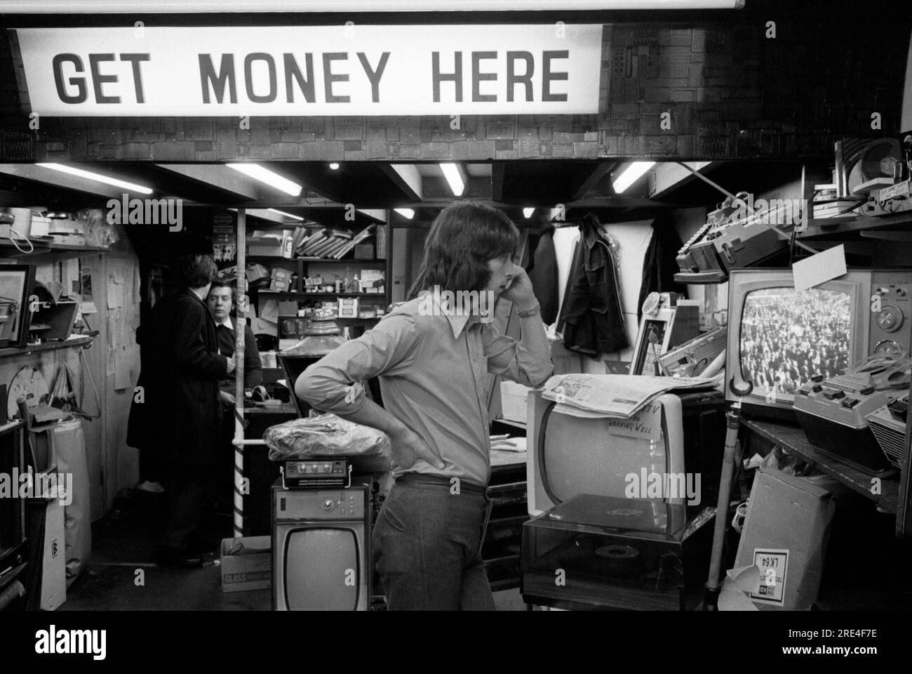 1970s television and radio repair secondhand shop UK. The sign reads 'Get Money Here' they also bought and sold secondhand TV sets, and other household electrical appliances, as well as repairing broken stuff . The man watching the TV is a salesman. Queensway, London. 1972  England HOMER SYKES Stock Photo