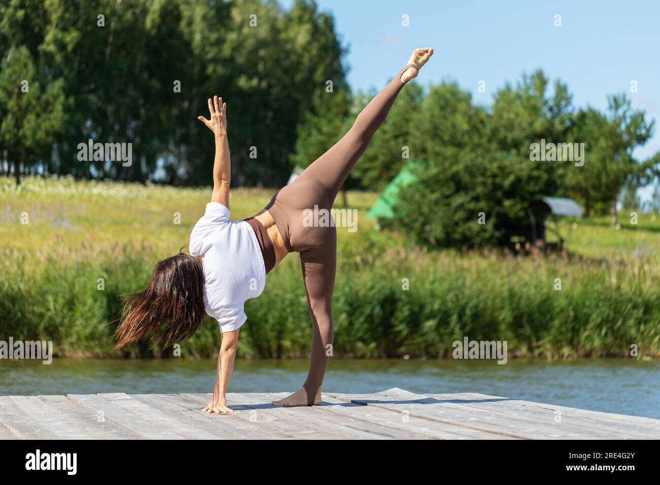 A woman leading a healthy lifestyle and practicing yoga, performs Ardha Chandrasana exercise, crescent moon pose, trains on a summer sunny morning on Stock Photo