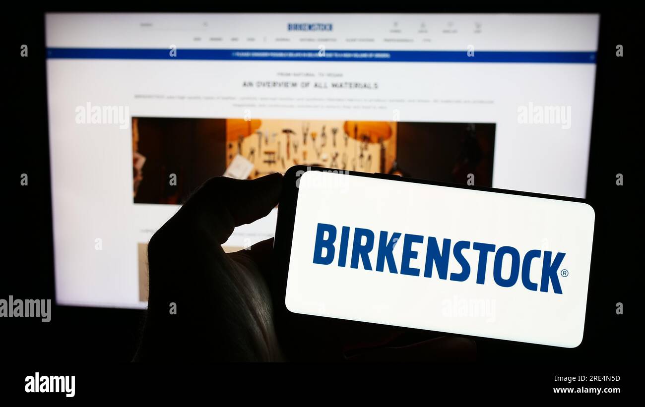 Person holding cellphone with logo of shoe company Birkenstock Group B.V. Co. KG on screen in front of business webpage. Focus on phone display. Stock Photo