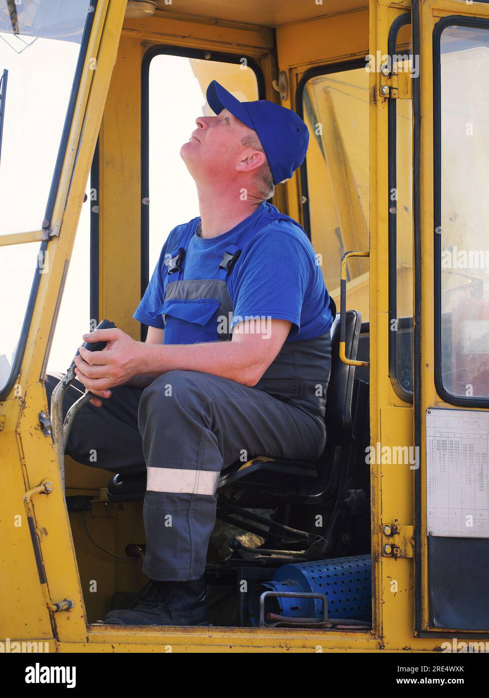 Crane operator sits in cab of crane and looks up. Driver of crane