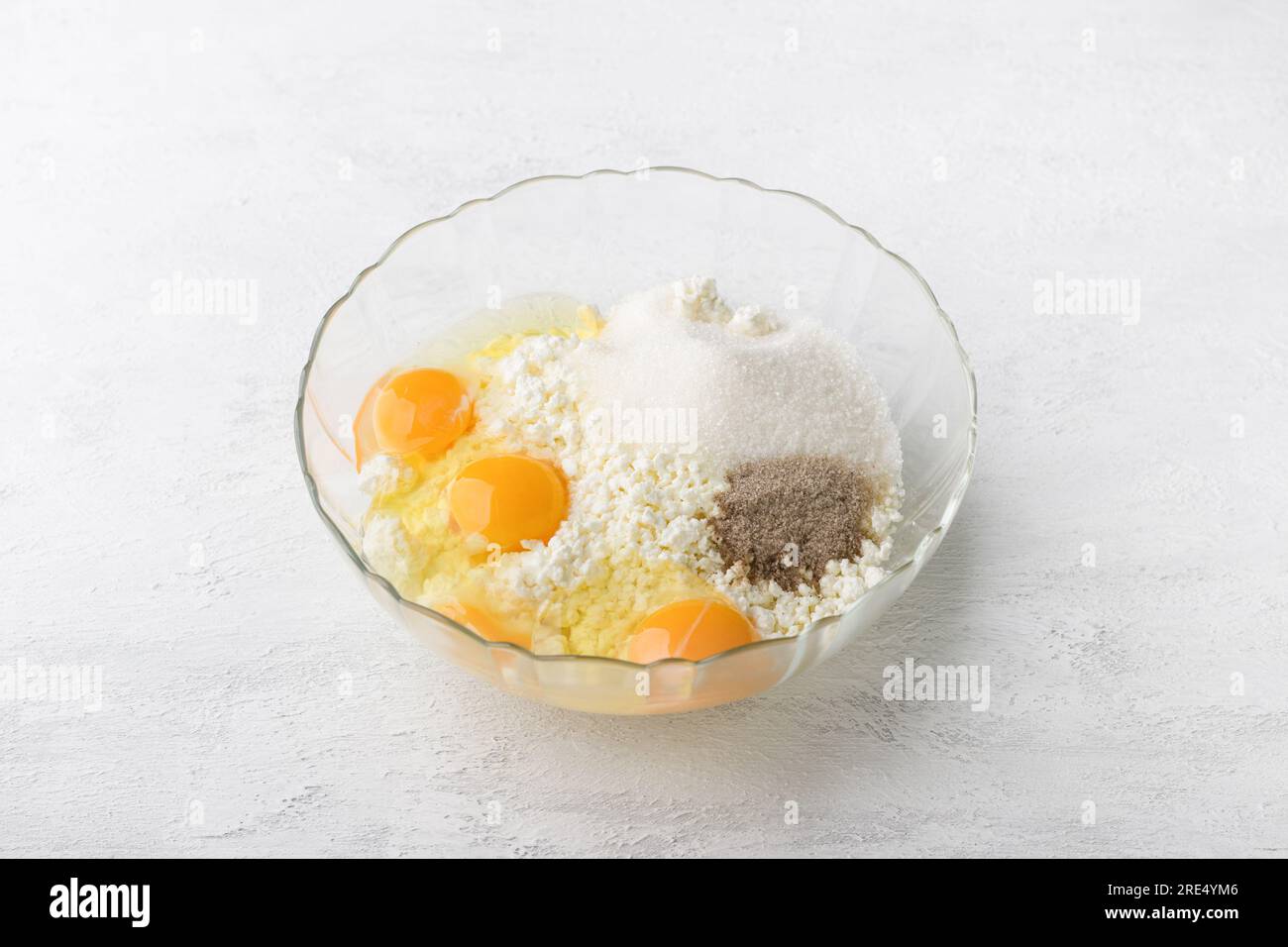 Glass bowl with a mixture of cottage cheese, eggs, sugar and vanilla sugar on a light gray background, cooking delicious homemade pastries, step by st Stock Photo