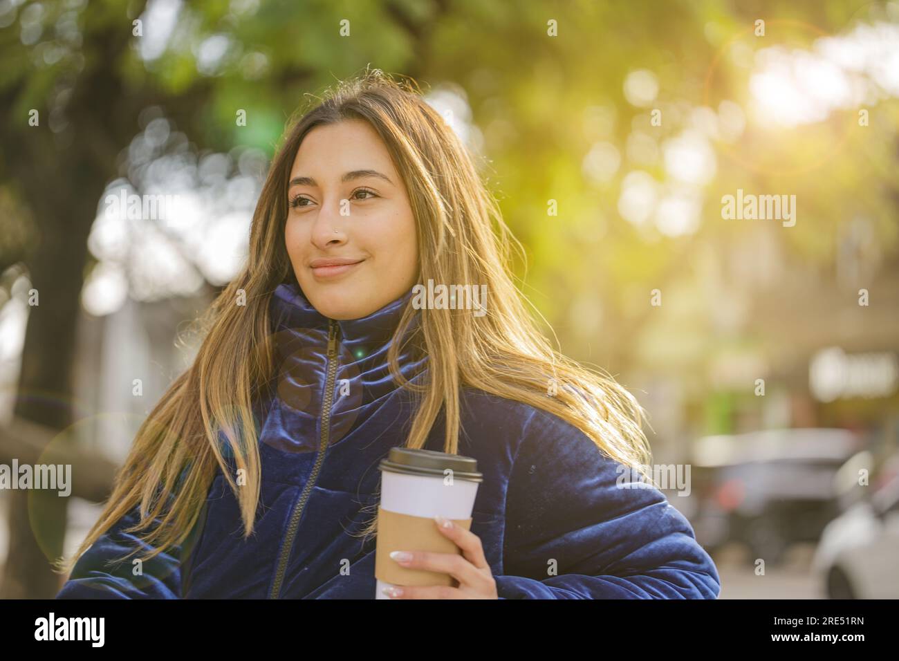 Latin girl drinking coffee sitting on a bench in a public park with copy space. Stock Photo