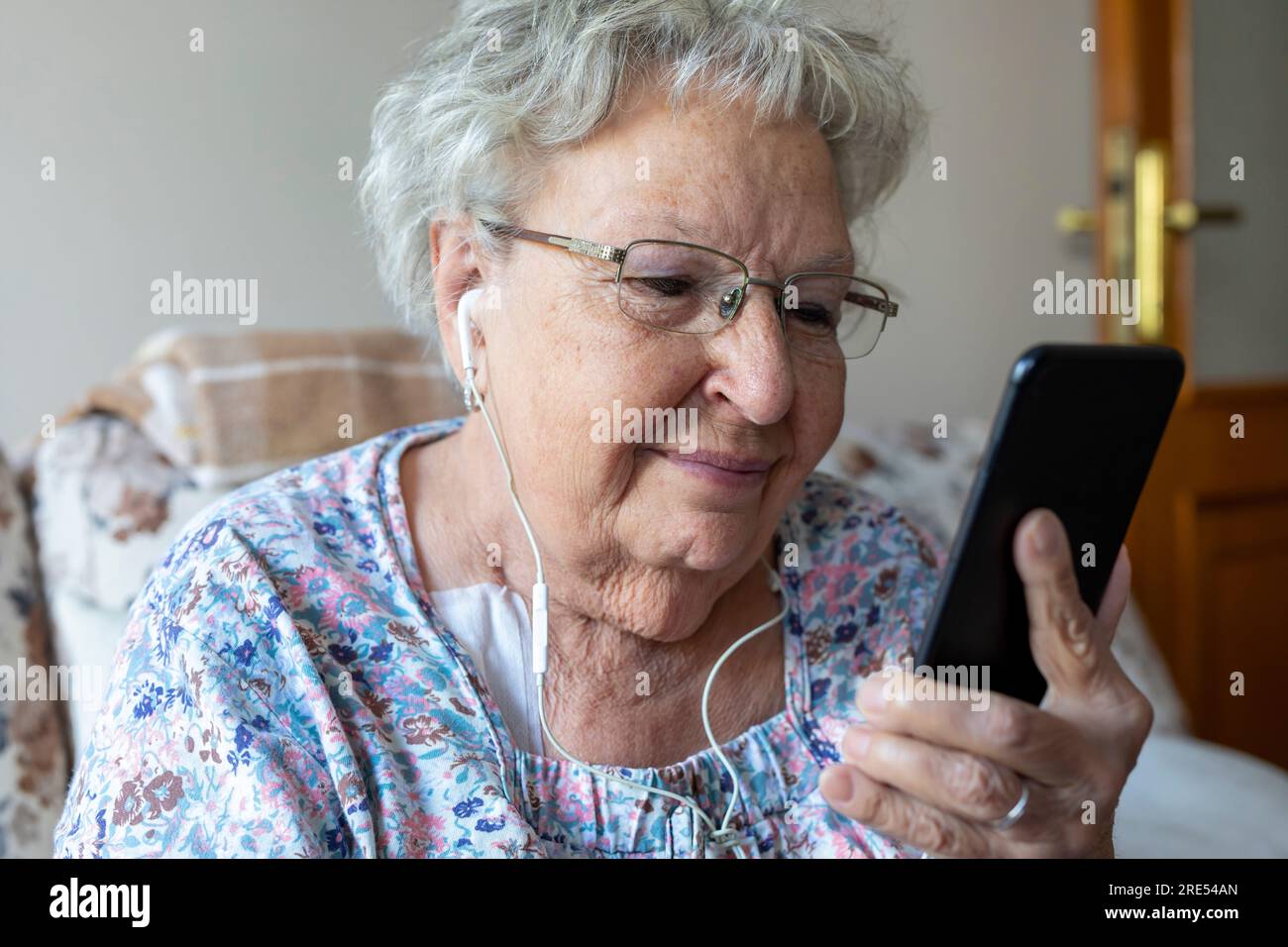 Happy elderly woman enjoying using mobile apps,  smiling senior woman holding smartphone, looking at mobile phone screen, browsing social media at hom Stock Photo