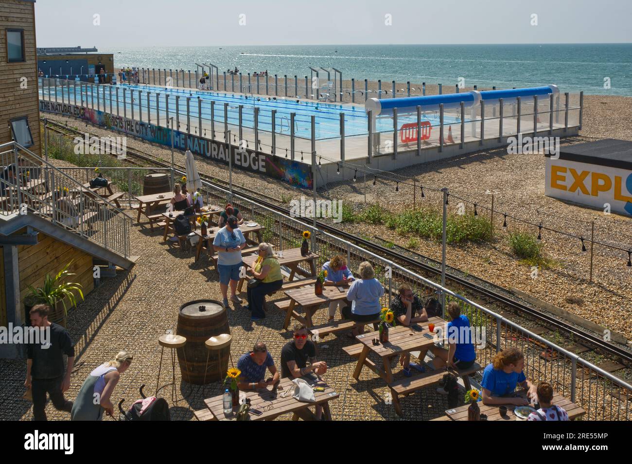 New swimming pool and cafe restaurant on shingle beach at Brighton, East Sussex, England. With people in pool and cafe. Stock Photo