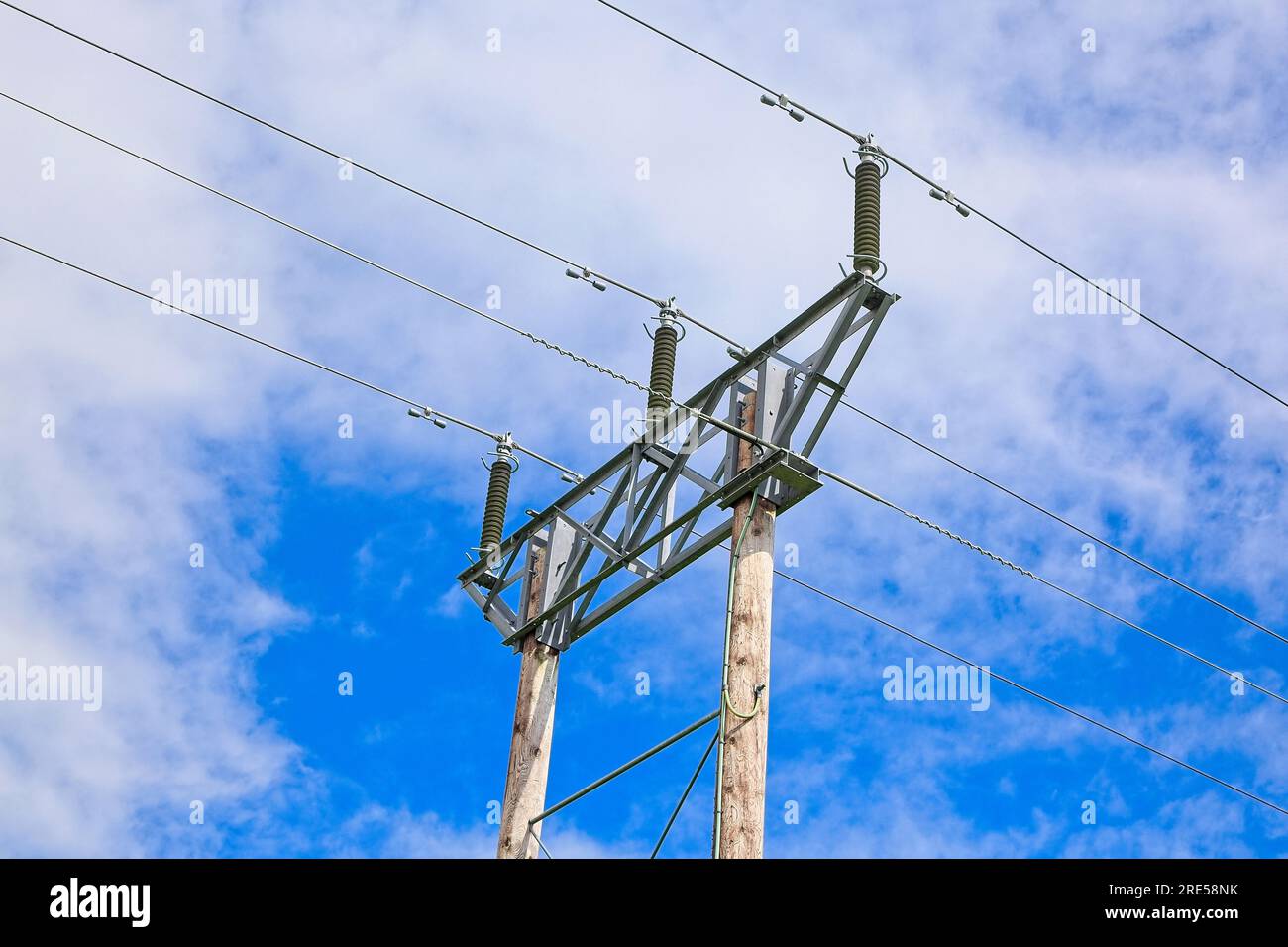 View looking up at power line cables on a metal frame and wooden polls Stock Photo