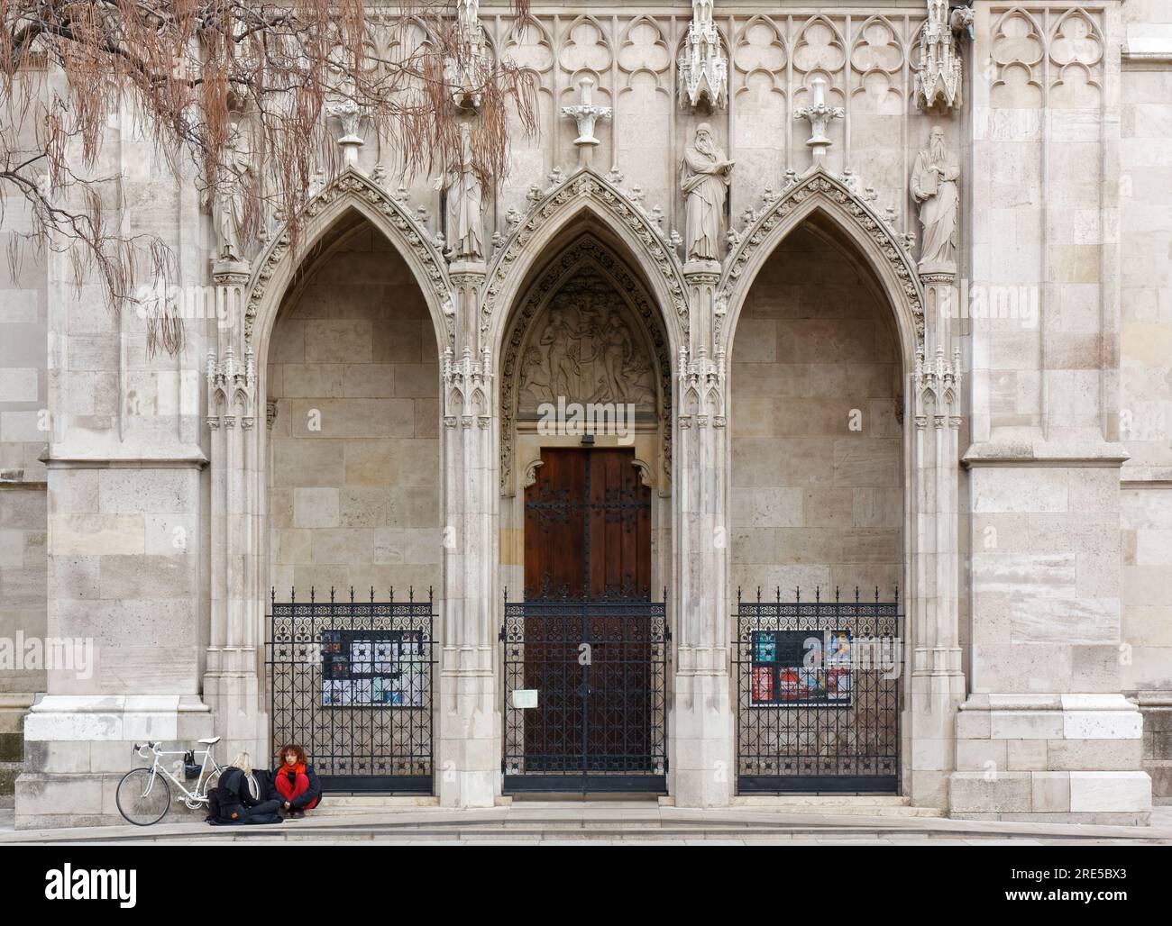 VIENNA, Austria - January 6, 2023: Two girls and a white bicycle in front of an entrance of the neo-gothic Votive Church Stock Photo