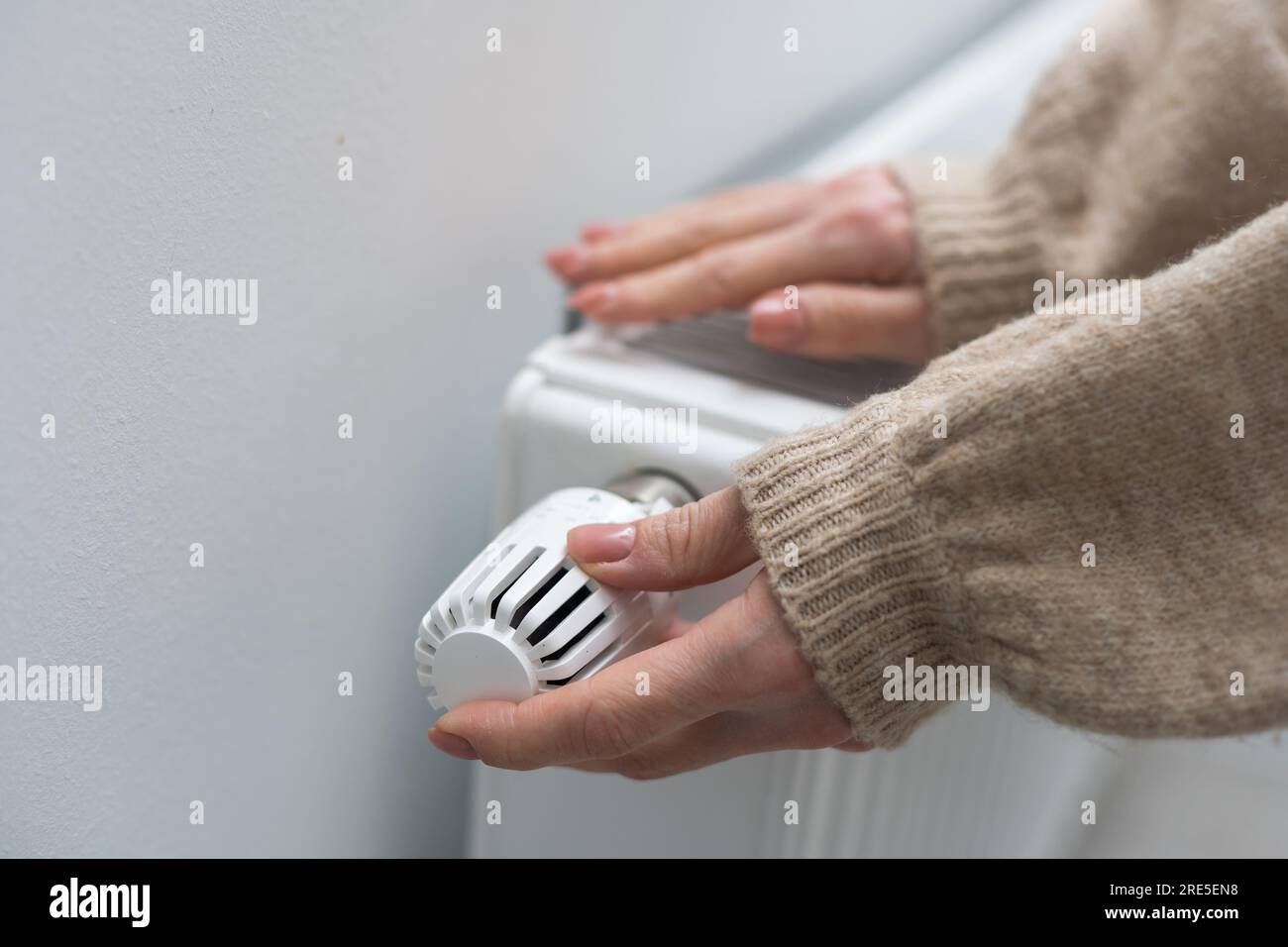 Female hands are trying to keep warm on an aluminum radiator. A woman warms herself near a radiator in winter during the energy crisis in Europe. Stock Photo