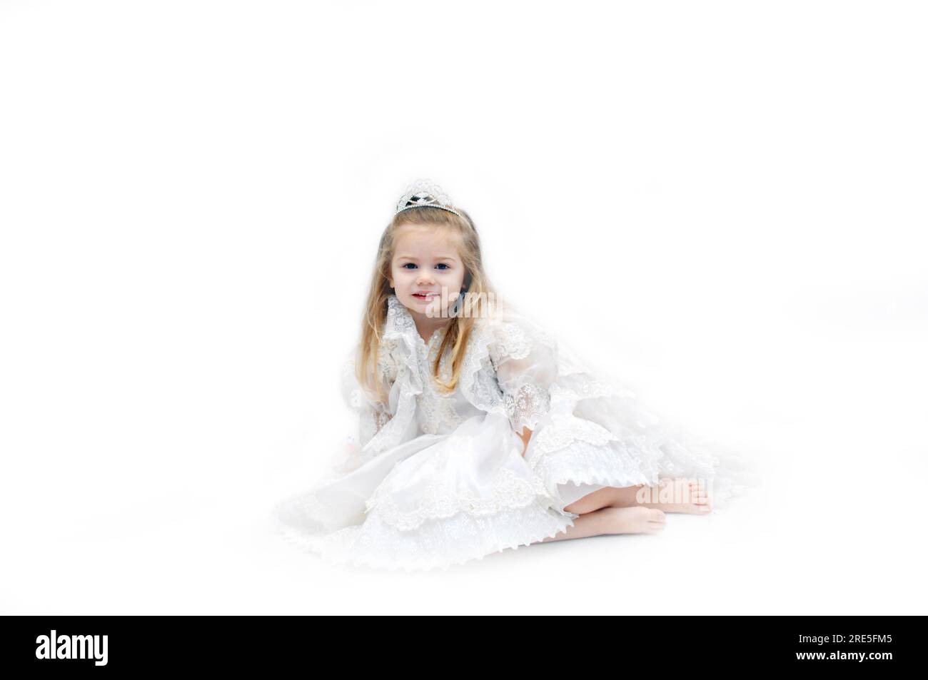 Angelic child dressed in all white lace and sparkling crown, sits in an all white room.  She is dreaming of being a bride one day. Stock Photo