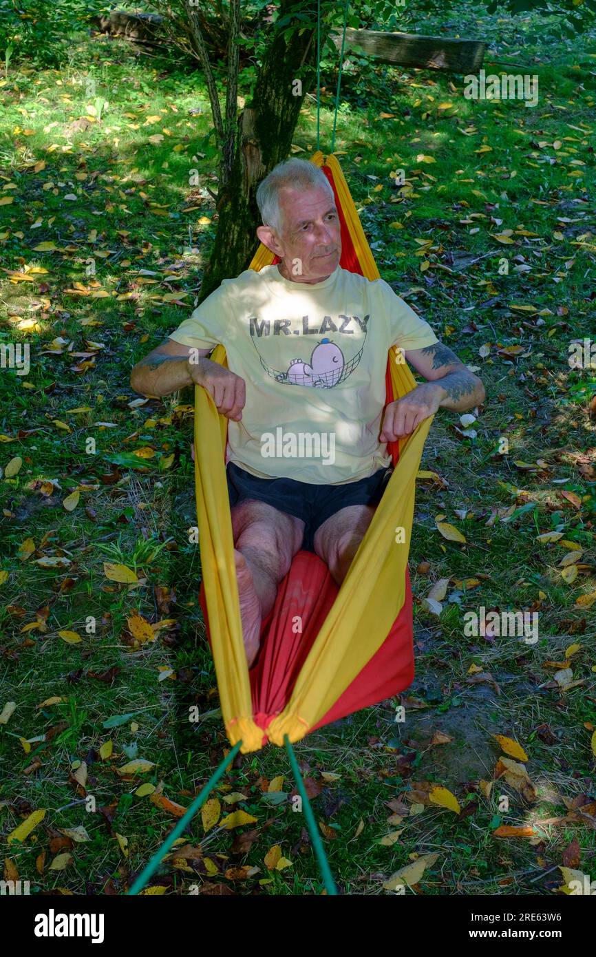 older man relaxing in garden hammock shaded by trees wearing mr lazy t.shirt zala county hungary Stock Photo
