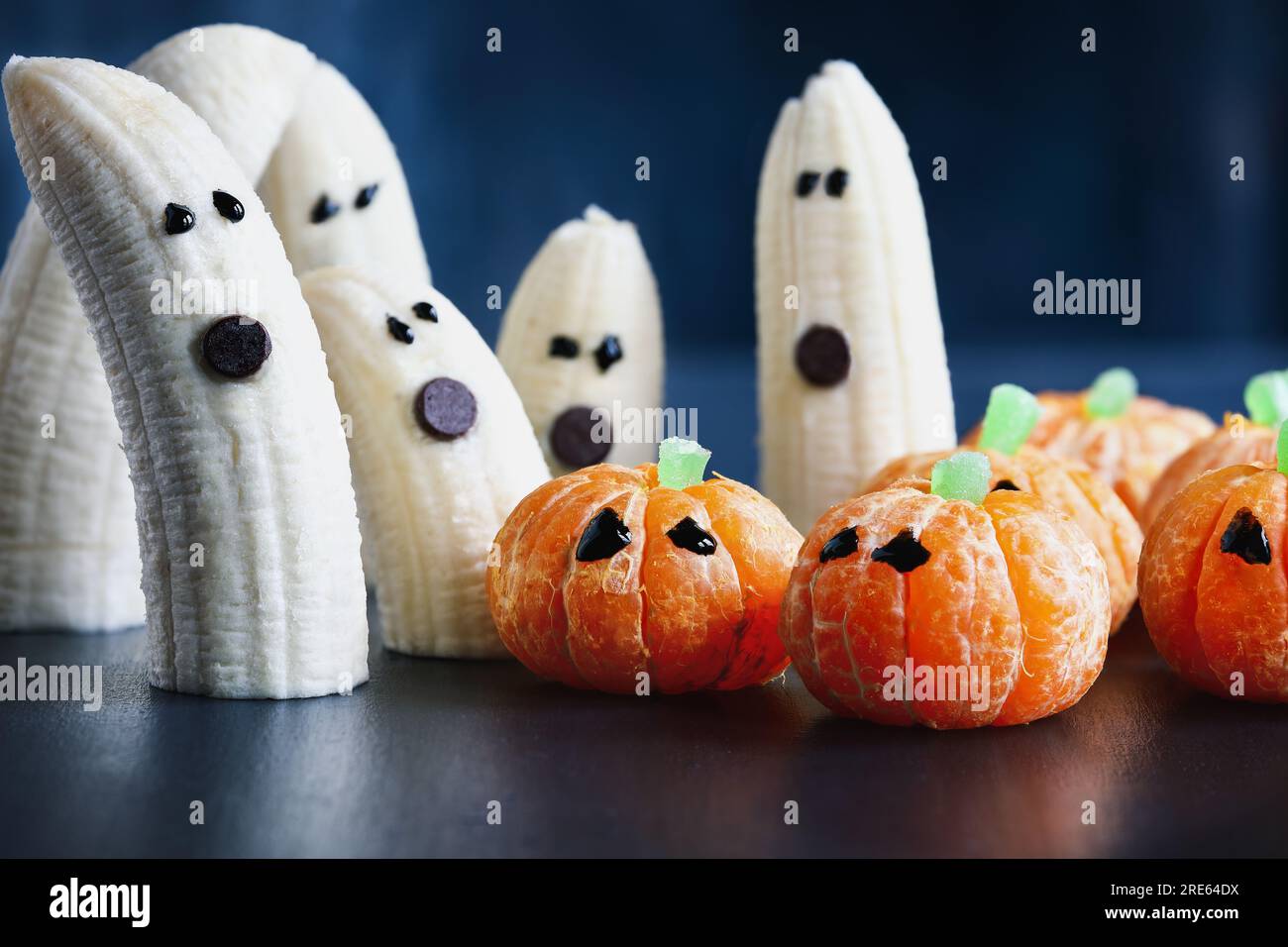 Halloween cute pumpkin orange fruit and scary banana ghosts monsters with chocolate faces. Healthy dessert snack with funny faces for child's party Stock Photo