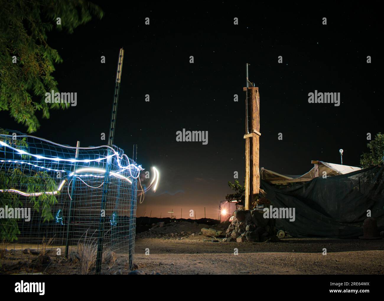 Night photography of random plants, fence, structures, and garden lights. With distant light pollution from a near by city lighting a star filled sky Stock Photo