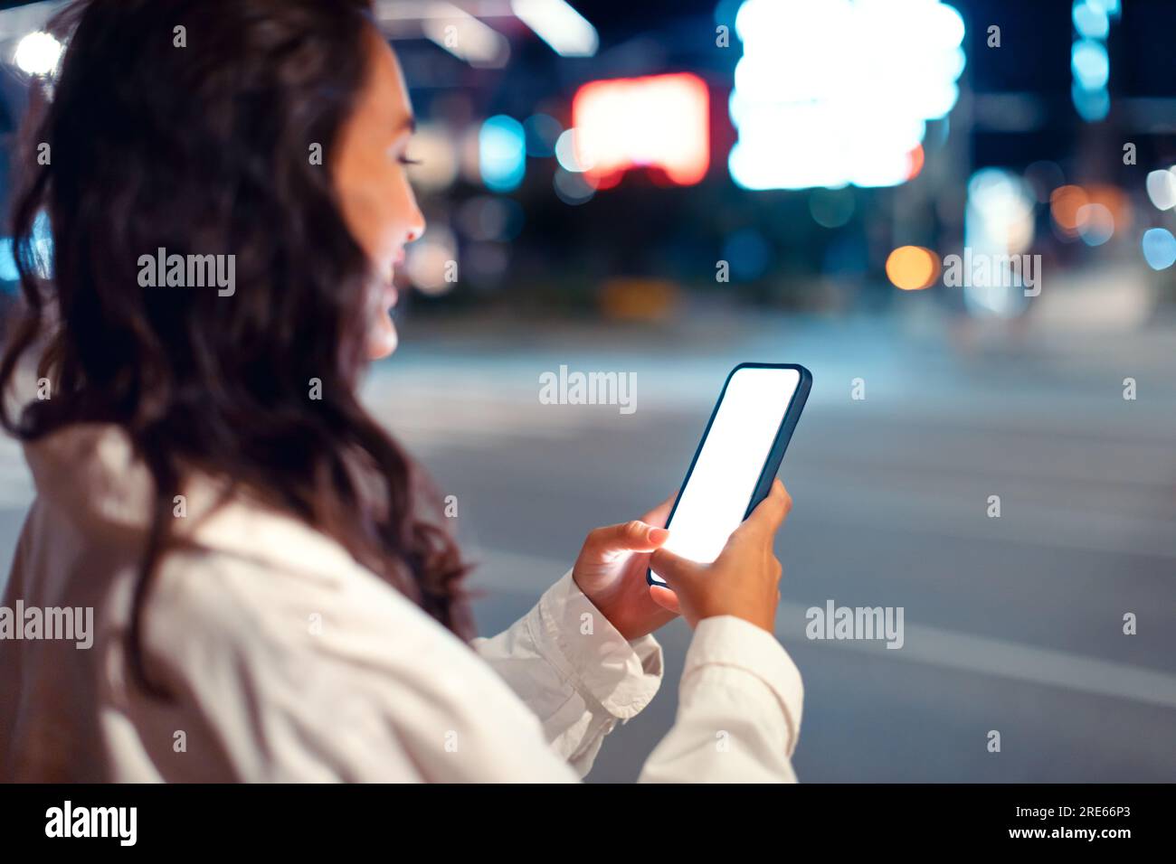 Young woman using smartphone with blank screen, standing at night city street near road, mockup, free space Stock Photo
