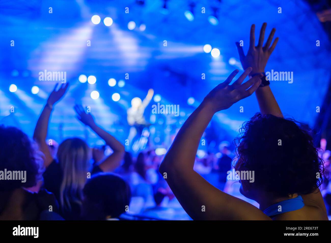 Back view of unrecognizable female with curly hair raising hands while ...