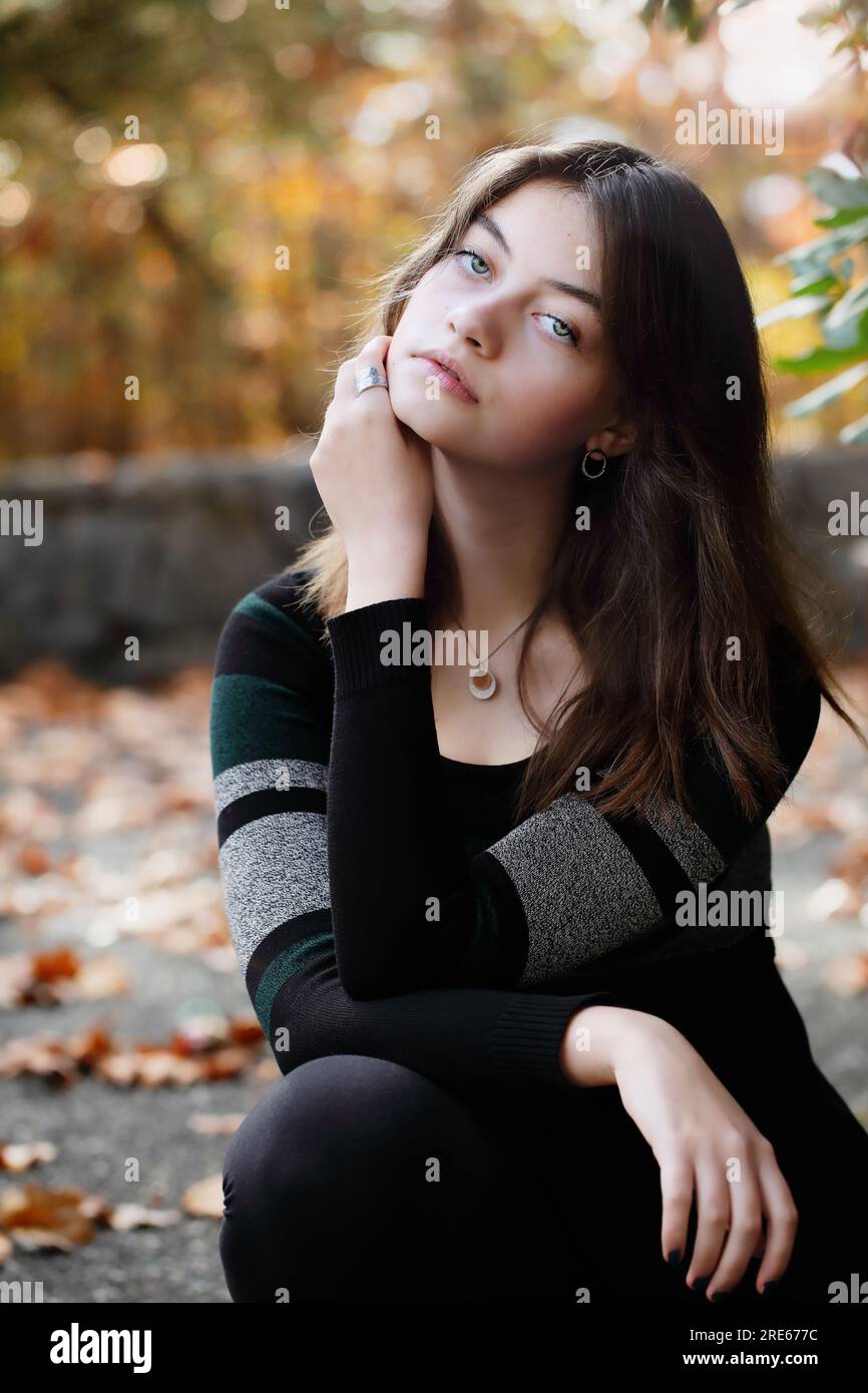 Beautiful brunette young woman thoughtfully looking into the camera surrounded by outdoor autumn colors. Selective focus with blurred background. Stock Photo