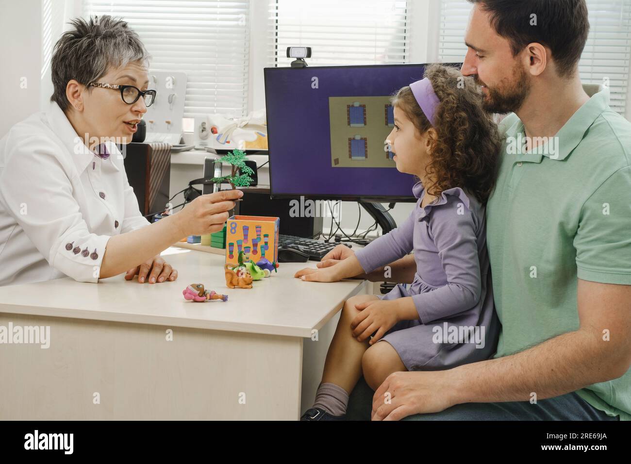 speech therapist working with child who has hearing problems. Rehabilitation teacher of the deaf consulting father with daughter. Speech therapist Stock Photo