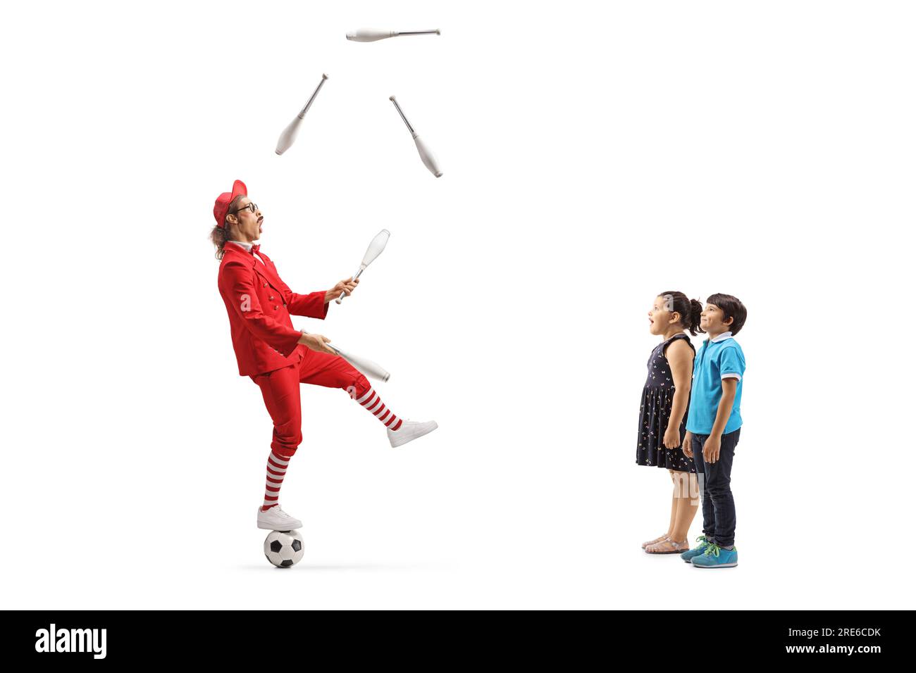 Kids watching a man in a red suit standing on a football and juggling isolated on white background Stock Photo